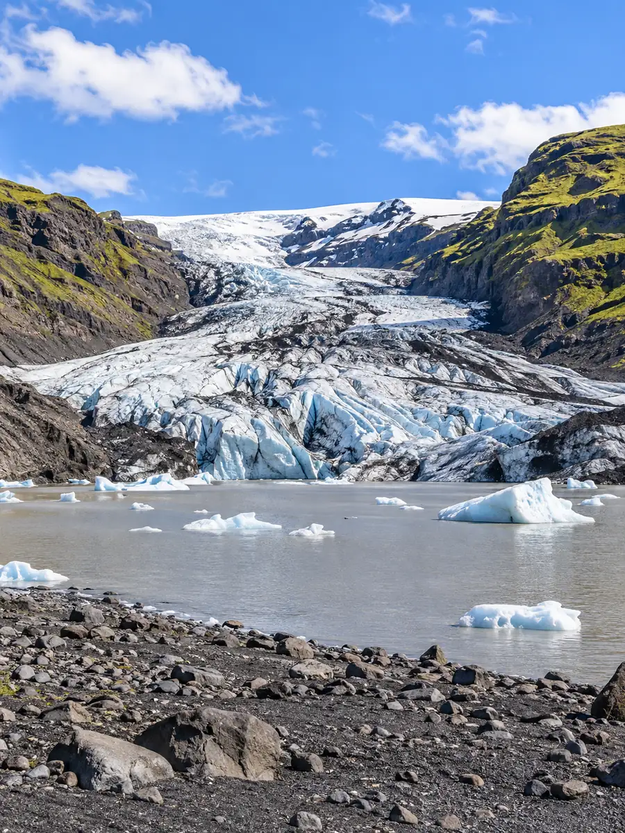 The Sólheimajökull glacier tongue rising from its grey lagoon with small icebergs between green-mossed slopes