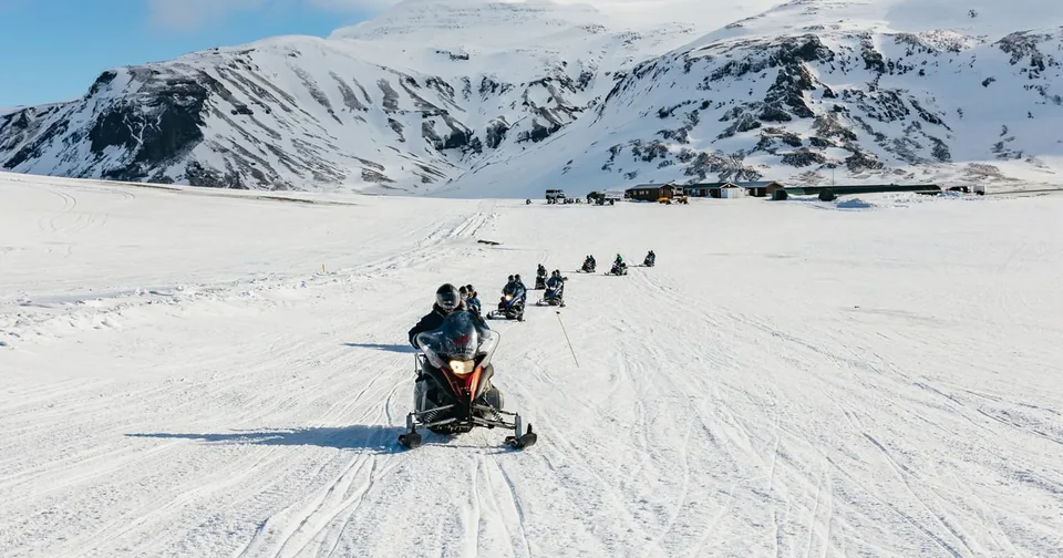 A line of snowmobiles crossing a white ice cap under a pale sky