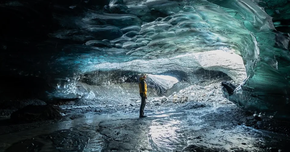 A group with helmets inside a wide Vatnajökull ice cave lit blue from above