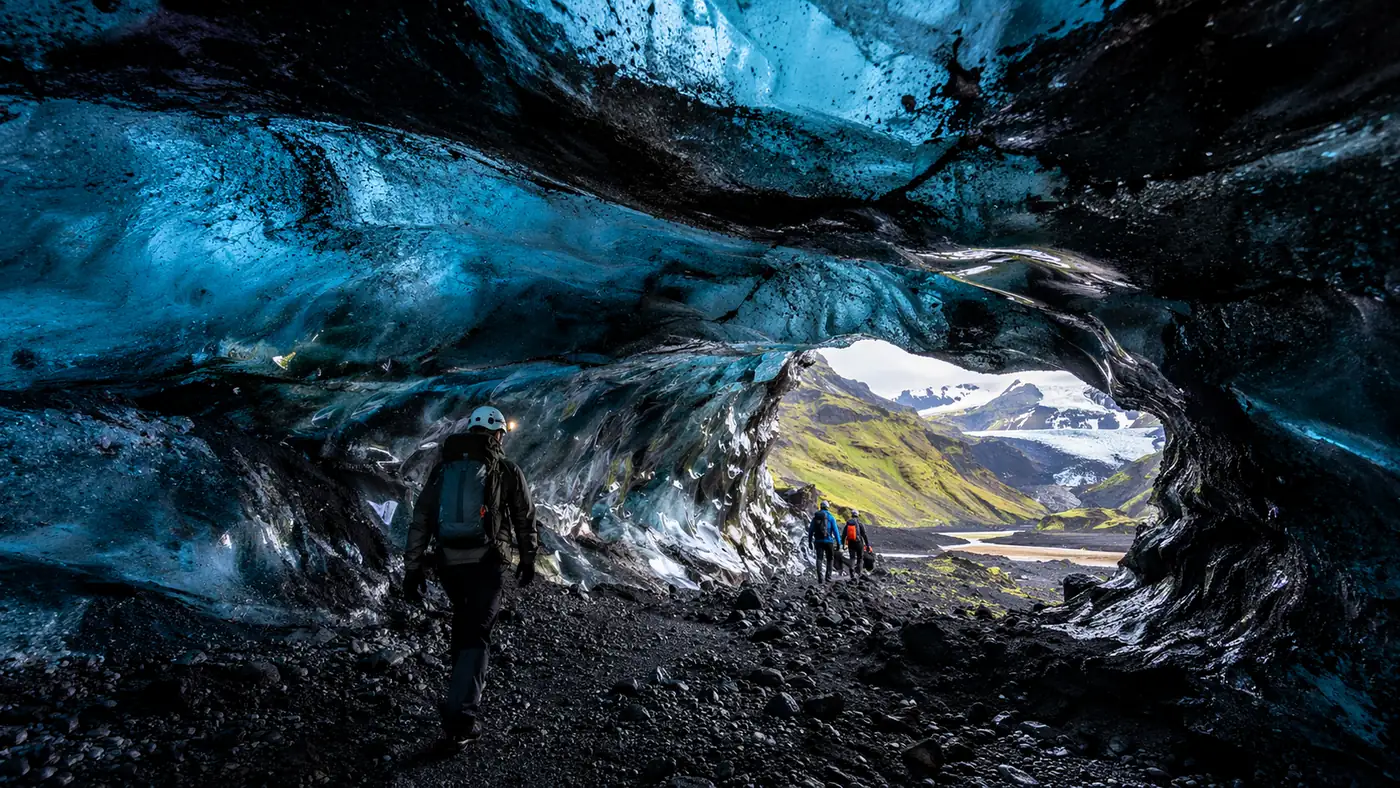 A black-and-blue ice cave with layers of volcanic ash frozen into the walls